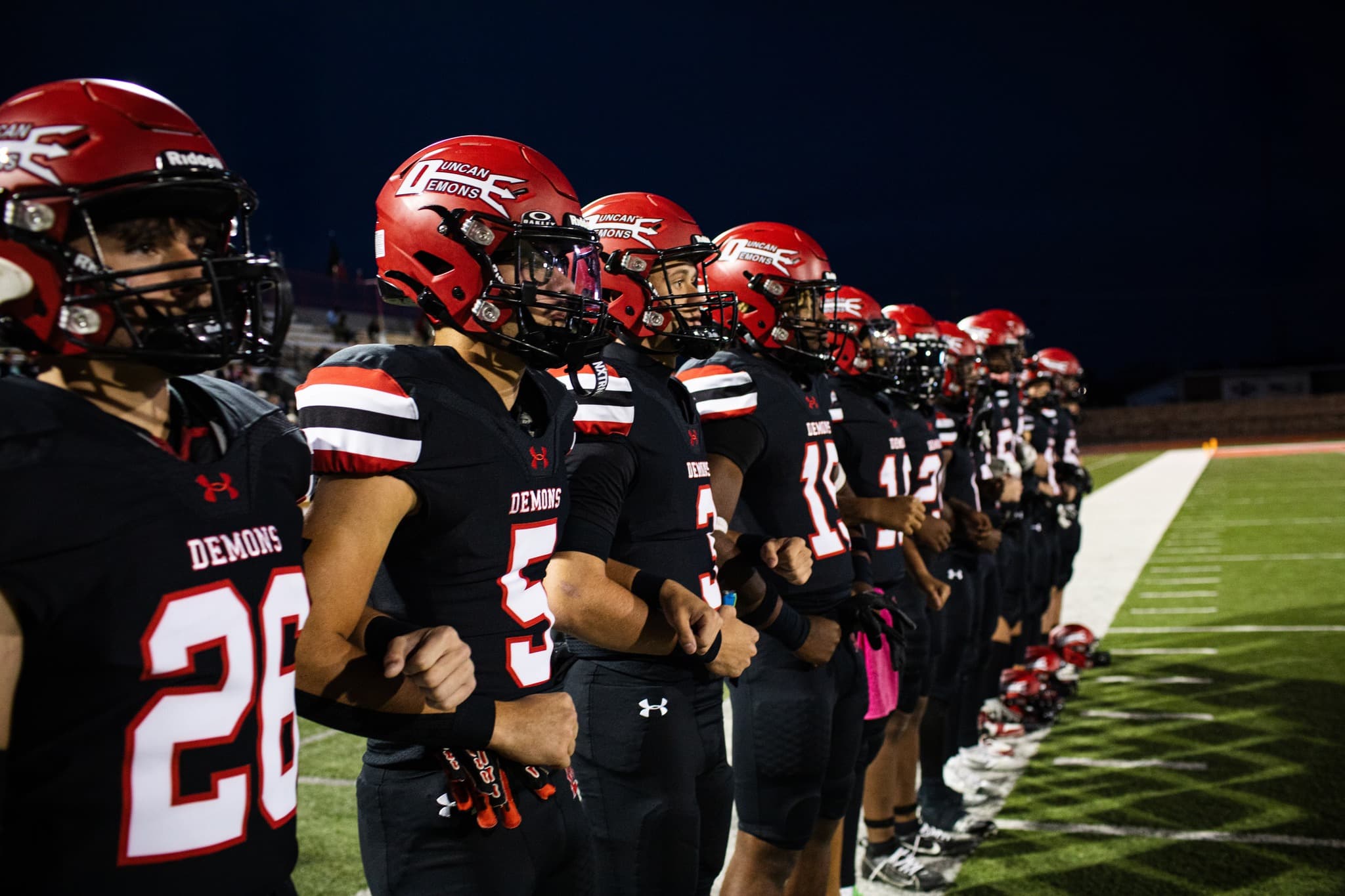 The team running out past cheerleaders with the video board lit behind them.